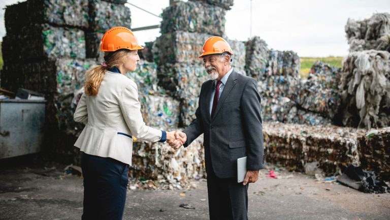 Two business people shaking hands in front of a pile of garbage, symbolizing a partnership amidst environmental challenges.