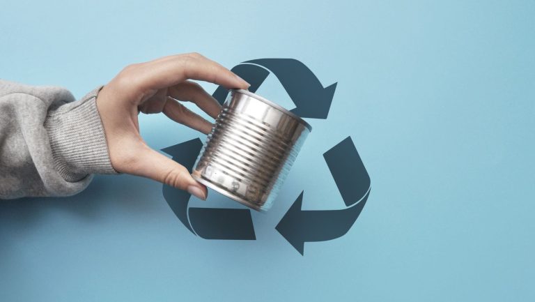 A hand holding a metal container with a recycling symbol behind it